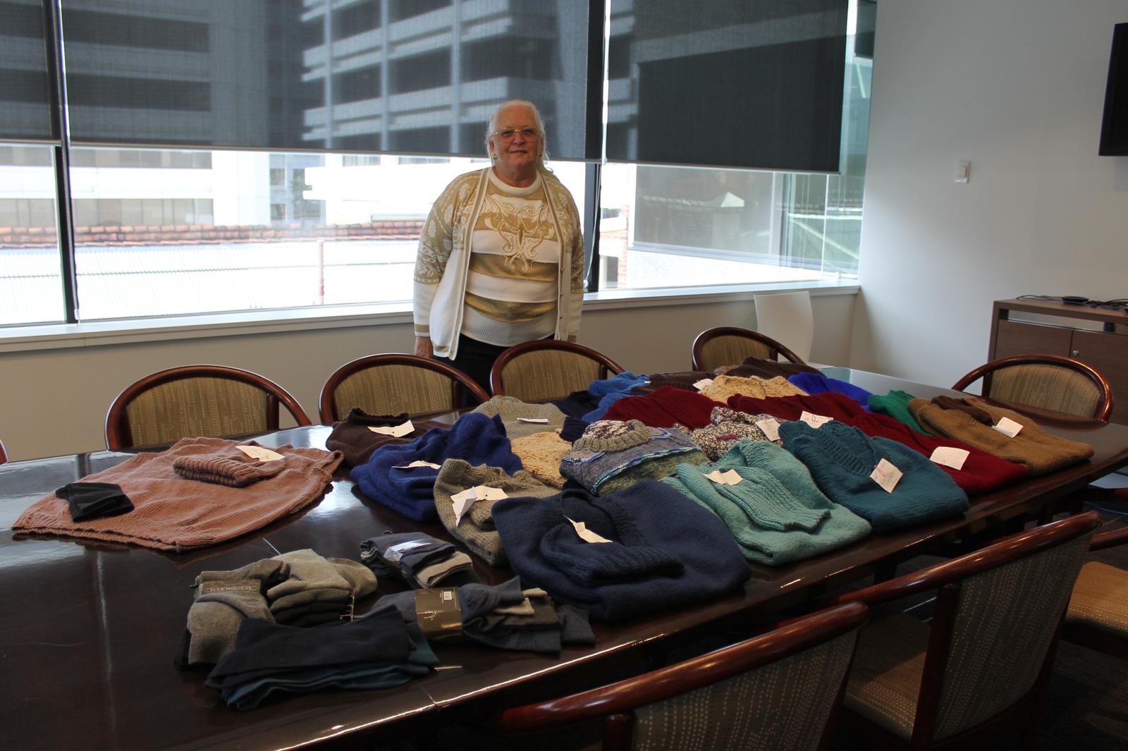 A volunteer poses with pullovers she & a team knitted for in need veterans.